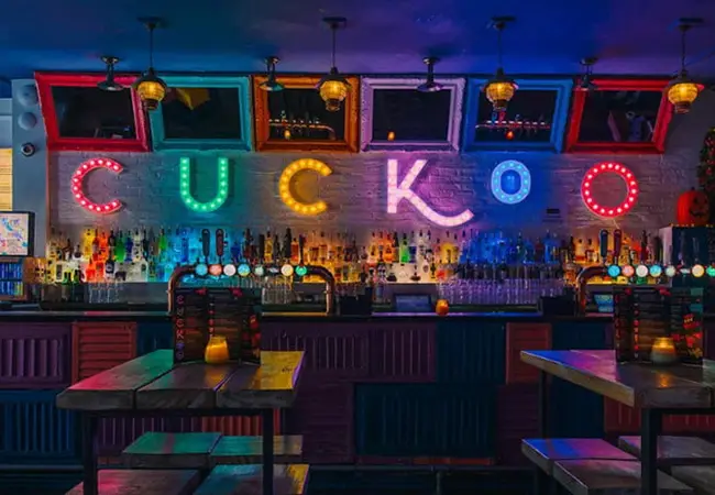 Guests enjoying the night scene at Cuckoo under the Neon Logo in one of Leeds' best bars on Call Lane.